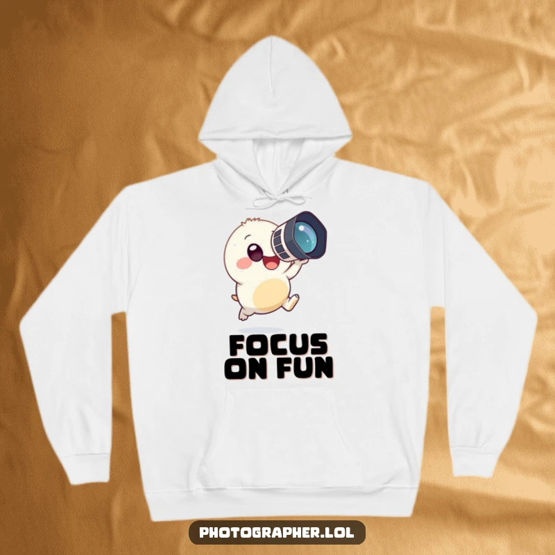 Funny, cozy hoodie depicting a small, round creature joyfully leaping with a large camera aimed, ready to capture the perfect, humorous shot.